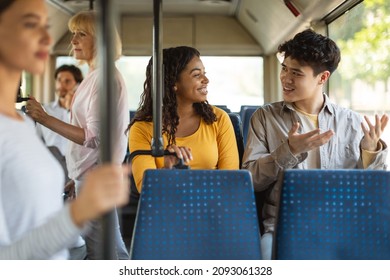 Public Transportation. Portrait of smiling African American young woman and Asian guy taking bus sitting on seat together, talking, enjoying travel or ride on public vehicle having conversation