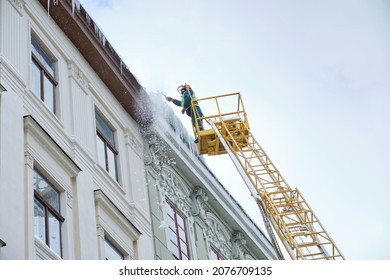 Public utilities on special vehicles remove icicles from the roofs of houses on the Rynok square in Lviv. Roof Winter Workers. Large icicles hanging from the roof