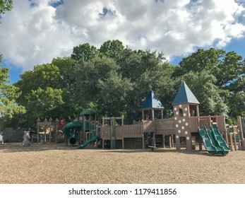 Public wooden children playground like fort or castle with separate sections for different ages. Play set structure under the lush of larger trees in Texas, USA, summer leaves green and cloud blue sky