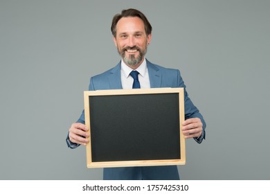 Publicity and education measures. Happy manager hold blackboard grey background. Bearded man smile with publicity board. Advertising and publicity. Advertisement design. School publicity, copy space.