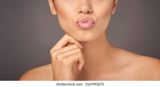 Pucker And Pout. Closeup Studio Shot Of A Woman With Gorgeous Glossy Lips Against A Gray Background.