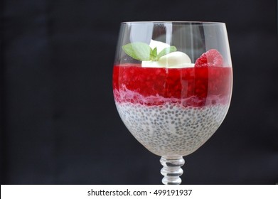 Pudding from chia seeds and raspberries with cottage with mint in glass on black background, front horizontal view