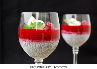 Pudding from chia seeds and raspberries with cottage with mint in glass on brown wooden background, front horizontal view