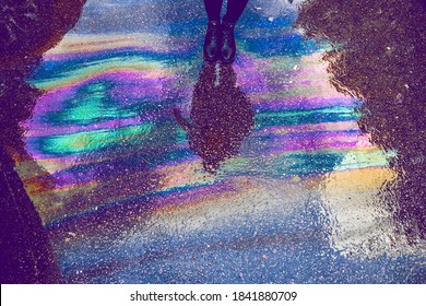 
a puddle of different colors from gasoline and a reflection of a black man there
