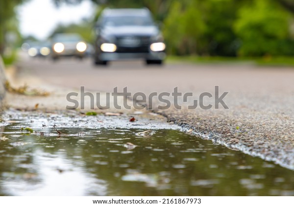A puddle next to a busy road with cars driving by\
after a rain storm