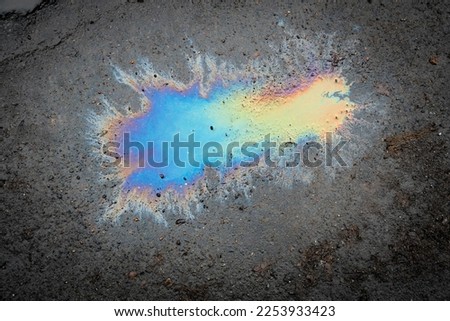 A puddle of spilled gasoline or oil product on the road. Environmental pollution conceptGasoline flows on the asphalt. Rainbow stains of oil and gasoline.