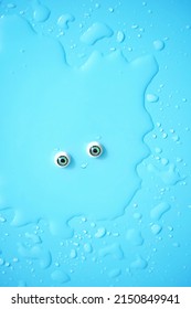 puddle, water drops texture and eyes close up on abstract blue background. funny face of water, unusual creature monster. minimal creative idea. flat lay