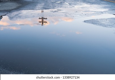 Puddle water reflection of sky clouds and power line. Above ground electricity pole reflected in urban setting background. Parking lot with abstract water puddle reflection - Powered by Shutterstock