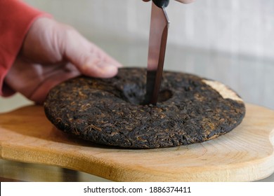 Puer tea cake on a wooden kitchen board.  The man cuts the tea.  Blurred hand movement.  - Shutterstock ID 1886374411