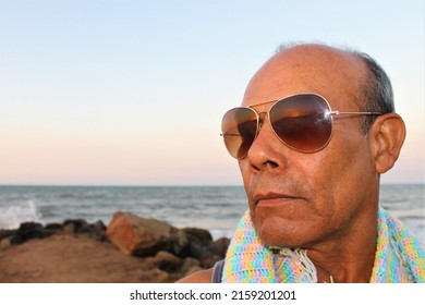 Puerto Píritu, Anzoategui, Venezuela. January 25, 2015. Close-up shot of a dark-haired older adult with sunglasses and a beach in the background.