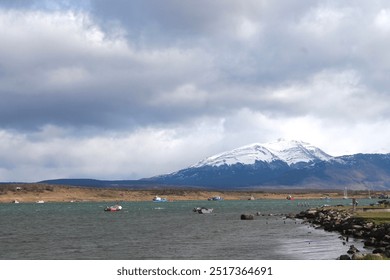 Puerto Natales.  Ocean fjord with many fishing boats in the water. Cloudy sky with snow capped mountains.  brightly colored small fishing boats in Patagonia, Magallanes, Chile. Magellan. Sub antarctic - Powered by Shutterstock