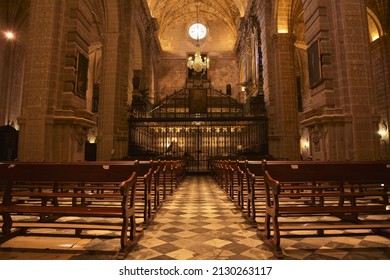 Puerto Santa María, Spain - Feb. 25, 2022: Impressive View Through Symmetrical Wooden Church Benches And Black White Tiled Checkered Floor Leading Up To The Barred Choir Area Of Iglesia Mayor Prior