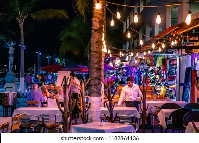 Puerto Vallarta Mexico 02/28/2017 Night Street Scene Of Restaurant Patio On Malecon With Waiter, Patrons And Pedestrians And Color.