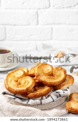 Puff. Flaky sugar Palmiers cookies in a ceramic plate on a light background. Sweet homemade cakes