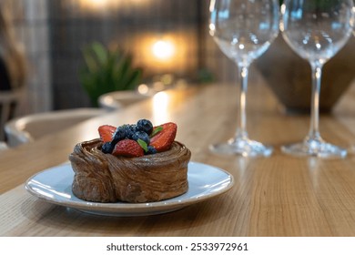 Puff with fresh strawberry and blueberry on plate and empty wine glasses on wooden table in cozy restaurant with romantic atmosphere. Pastry with berries in cafe. Sweet dessert - Powered by Shutterstock