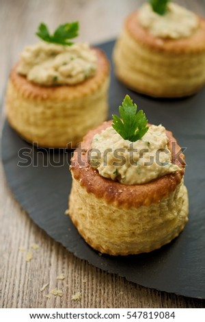 Puff pastry bouchees dough cups filled with tuna spread and garnished with parsley. Concept of amuse bouche. Selective focus on front parsley leaf.