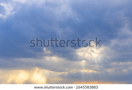 Puffy clouds float in the evening sky as sunlight filters through, creating a captivating interplay of light and shadow. The atmosphere feels serene and enchanting during this twilight hour.