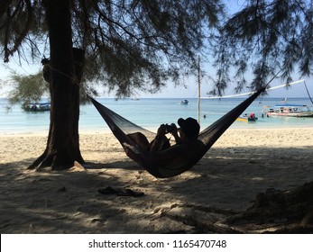 Pulau Perhentian Malaysia 21 July 2018 :Traveler guy is relaxing in a hammock hang on tree directly on the beach.Man take a chilling moment during adventure vacation and enjoy the beauty of the Nature