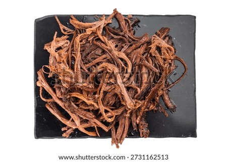 Pulled beef brisket jerky on black serving plate, dried meat snack close up, high protein carnivore food concept