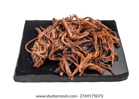 Pulled beef brisket jerky on black serving plate, dried meat snack close up, high protein carnivore food concept