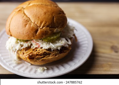 Pulled Pork BBQ Sandwich With Sweet Pickles And Coleslaw On A White Plate. 