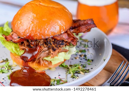 A Pulled Pork Burger with bacon, lettuce and barbecue sauce in a bead bun