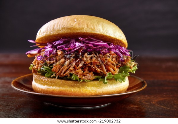 Pulled pork burger with red cabbage salad and\
bbq sauce on plate with dark background\
