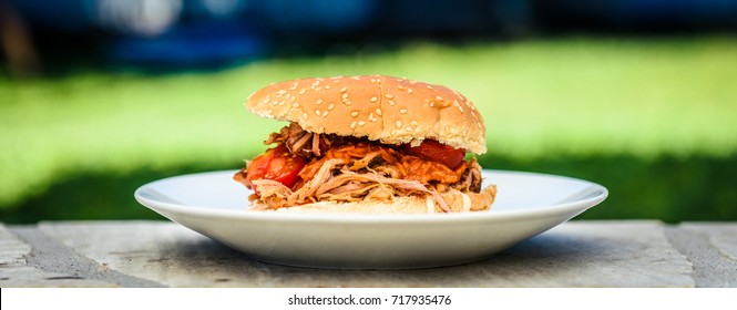 Pulled pork sandwich burger is served with nature background. Home made pulled pork made in house oven, smoker or barbecue bbq is served in a burger bun and served in the nature.