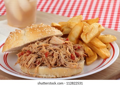 Pulled Pork Sandwich On A Sesame Seed Bun With French Fries On A Plate