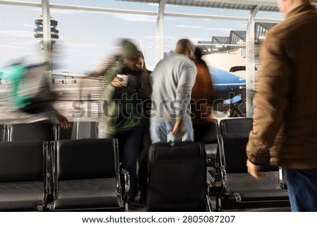 Pulling luggage, fast motion blur and hectic travelers in busy airport terminal, rushing, chaotic traffic flow and passengers walking inside modern crowded airport lounge.