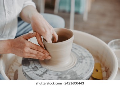 Pulling out the walls of a clay product on a potter's wheel. Hands of a Ceramist creating pottery from white clay. Close-up - Powered by Shutterstock
