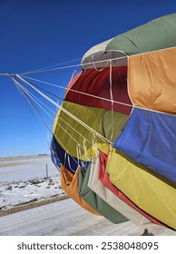 Pulling the parachute out of the top of a multi colored hot air balloon after it has landed in order to deflate the balloon.