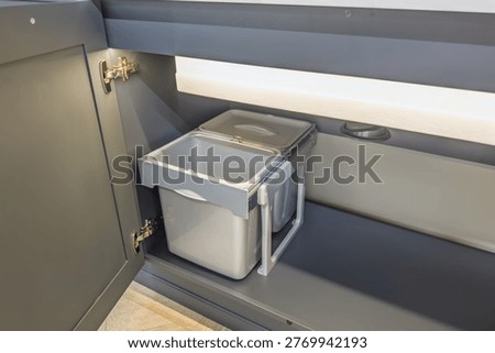 Pull-out kitchen waste bins with lids inside a grey cabinet.