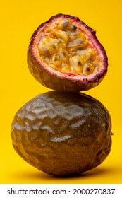 Pulp flesh showing in cut open Maracuja or Brazilian tropical passion fruit on top of another. Studio still life against a yellow background