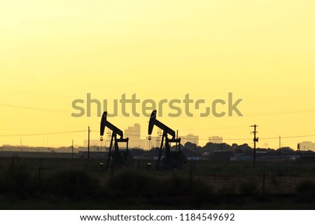 pump jack silhouettes against city skyline and golden light