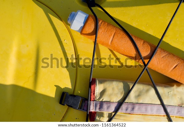Pump and paddle float strapped on deck of\
yellow sea kayak in\
sunlight.