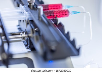 Pump pushing red liquid medium through syringes and flexible tubes in a small chip devise for an experiment in a scientific laboratory.