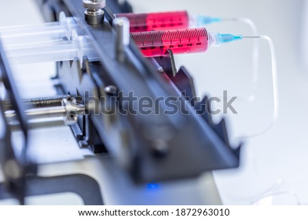 Pump pushing red liquid medium through syringes and flexible tubes in a small chip devise for an experiment in a scientific laboratory.