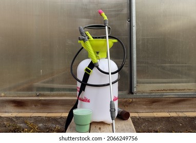 pump sprayer against the background of a closed greenhouse and a solution of Bordeaux liquid in a plastic glass