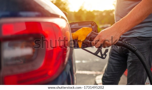 Pumping gas at gas pump. Closeup of\
man pumping gasoline fuel in car at gas station. Gas pump nozzle in\
the fuel tank of a blue car, refuel. Petrol pump\
filling