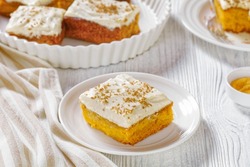 Pumpkin Cake With Cream Frosting In Baking Pan And One Slice On A White Plate, On White Wooden Table, Landscape View From Above