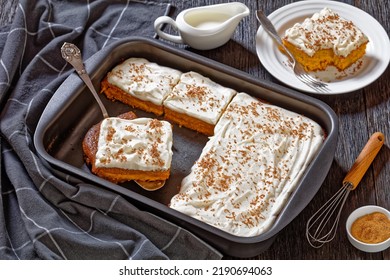 pumpkin cake with cream frosting in baking pan and one slice on a white plate, horizontal view from above