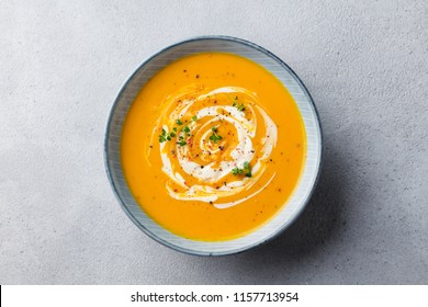 Pumpkin and carrot soup with cream on grey stone background. Close up. Top view.
