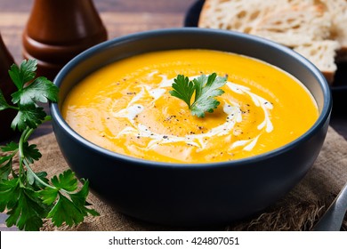 Pumpkin and carrot soup with cream and parsley on dark wooden background