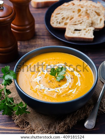 Pumpkin and carrot soup with cream and parsley on dark wooden background