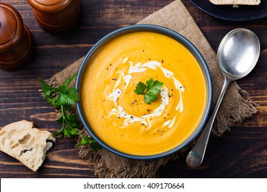 Pumpkin and carrot soup, tadka with cream and parsley on dark wooden background. Top view.