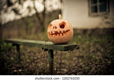 Pumpkin with carved eyes and mouth on old wooden bench on background of ruins of house. Decor for Halloween.