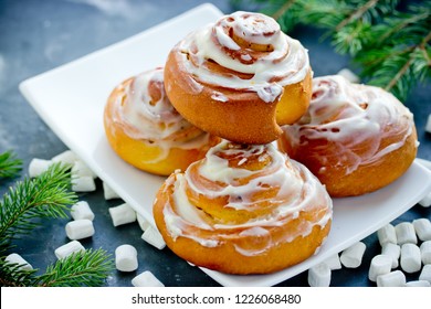 Pumpkin Cinnamon Rolls With Cheese Frosting On Dining Table With Christmas Tree Branches And Marshmallow