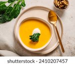 Pumpkin cream-soup served spinach, nuts, sour cream. Tasty Homemade Pumpkin, Sweet Potato or Carrot Soup in Bowl on Neutral Pastel Background. Cozy autumn comfort food. Top view