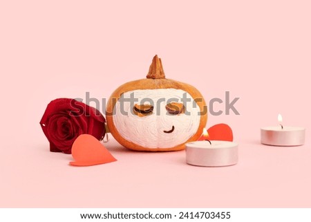 Pumpkin with drawn face, candles, paper hearts and clay mask on pink background